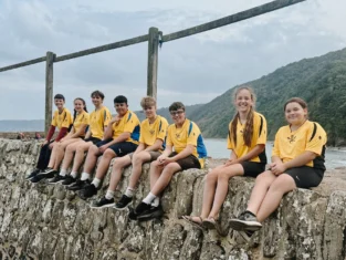 Junior Boscastle and Crackington rowing crew sit on harbour wall, beach in background